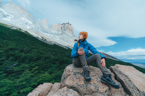Young Caucasian woman with yellow backpack looking  at scenic view of Torres del Paine National Park in Chile