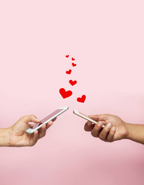 Online Dating Man and woman holding smart phones on pink background. Sending heart shape. heart emoji phone stock pictures, royalty-free photos & images