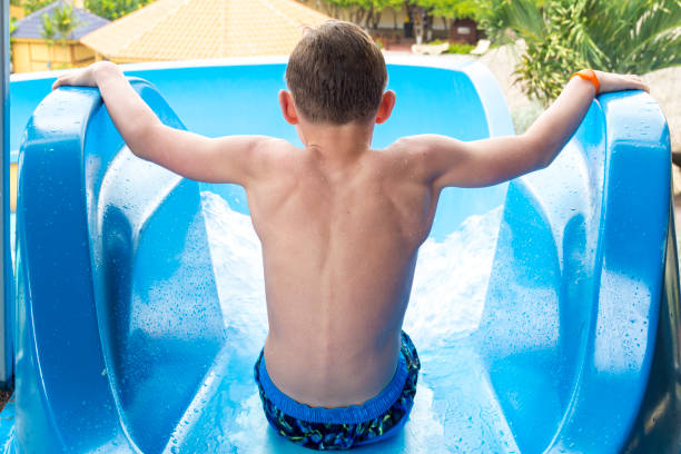 Boy at the Top of a Waterslide at Resort Hotel This picture shows the rear view perspective of a boy about to launch himself down a waterslide. This slide was found at a resort hotel. top of water slide photos stock pictures, royalty-free photos & images