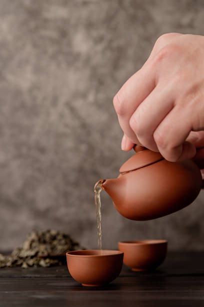 istock male hand pouring tea into tea cup front view on dark background 1196061258