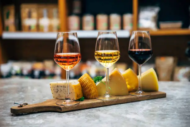 Photo of Glasses of Wine and cheese. Assortment or various type of cheese, wine glasses and bottles on the table in restaurant. Red, rose and yellow wine or champagne on the table. Winery concept image