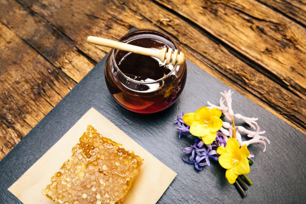 miel sain, naturel, organique et doux dans un bocal ou un bol en verre avec une trempette au miel, des fleurs et un nid d'abeilles sur fond noir. - breakfast stick honey meal photos et images de collection