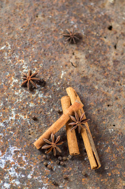 palos de canela, estrellas de anís y granos de pimienta negra sobre fondo texturizado - cardamom spice cinnamon bark anise star fotografías e imágenes de stock