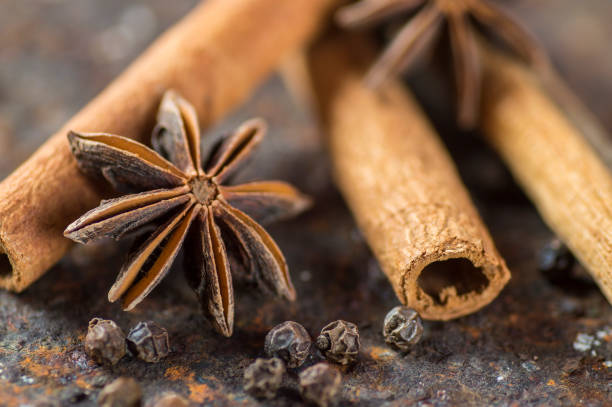 palos de canela, estrellas de anís y granos de pimienta negra sobre fondo texturizado - cardamom spice cinnamon bark anise star fotografías e imágenes de stock