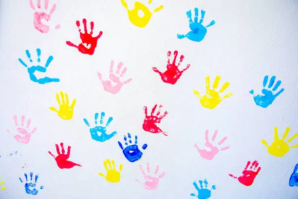 Photo of Colorful hand prints of hands isolated on white wall background. Children's handprints on school wall