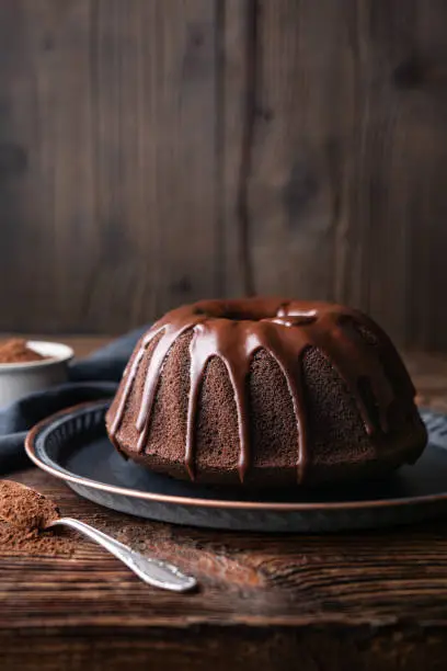 Delicious dessert, dark chocolate bundt cake topped with ganache glaze on rustic wooden background with copy space