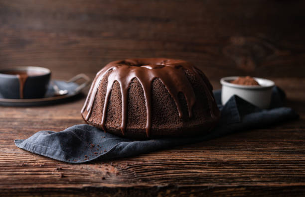 Delicious dessert, dark chocolate bundt cake topped with ganache glaze Delicious dessert, dark chocolate bundt cake topped with ganache glaze on rustic wooden background dessert topping photos stock pictures, royalty-free photos & images