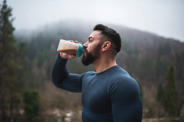 Sportsman Drinking Protein Outdoor Sportsman drinking protein in shaker bottle outdoor in front of foggy hill in autumn season, close up, drinking water after outdoor exercise. cocktail shaker stock pictures, royalty-free photos & images