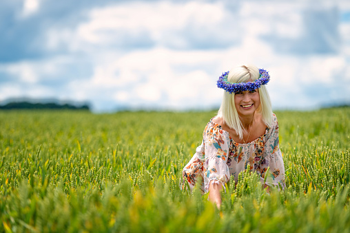 Beautiful, attractive, blonde woman with cornflower blue crown in the field of cereals.