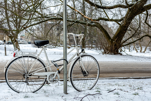 White bicycle with lock locked at street sign. City winter landscape.