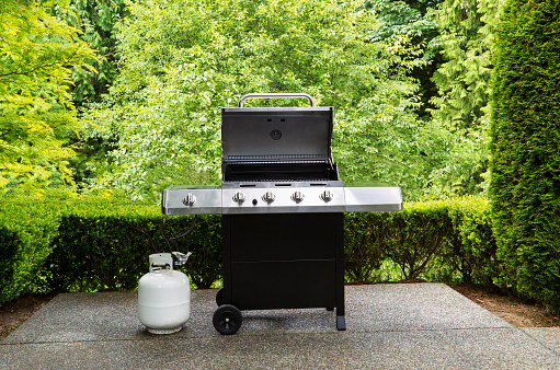 large barbeque cooker, with lid up, on concrete outdoor patio with woods in background