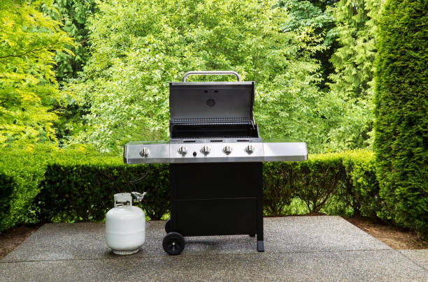 Large outdoor bbq cooker with lid in open position on home concrete patio large barbeque cooker, with lid up, on concrete outdoor patio with woods in background propane photos stock pictures, royalty-free photos & images