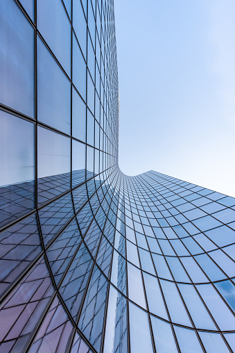 Blue curved glass skyscraper facade reflections against sky