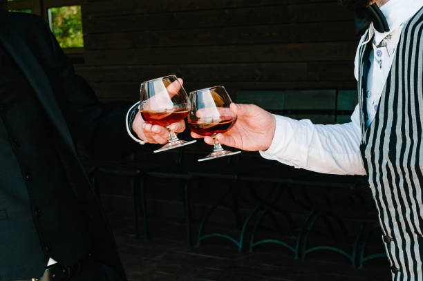 à votre santé! fermez-vous vers le haut de deux hommes célèbrent et lèvent des verres de boisson alcoolisée de boisson de whisky dans le pub. verres de rhum. les hommes d'affaires passent du temps ensemble à boire du brandy. - whisky cocktail glass rum photos et images de collection