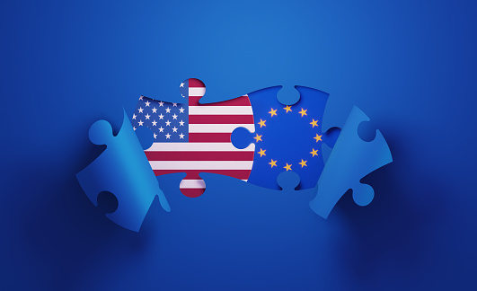 Jigsaw puzzle pieces textured with American and European Union  flags. Horizontal composition with copy space and selective focus. Solution concept