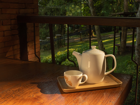 Stoneware teapot and tea cup on a wooden tray put on the wooden table in a natural right in the morning.
