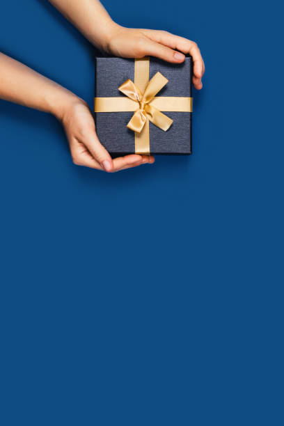 Hands with a gift box. Gift box with surprise in a female hands on classic blue background. Flat lay, top view, place for text. hand holding gift stock pictures, royalty-free photos & images