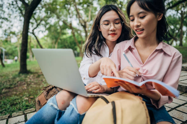 istock Students sitting in park with laptop 1196164711