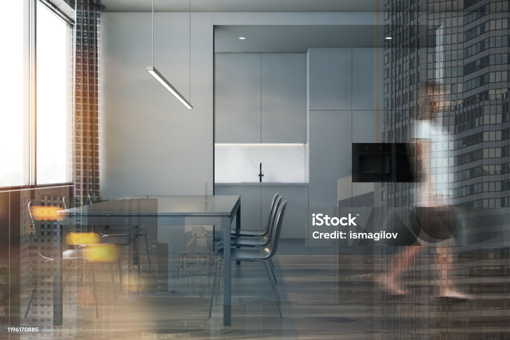 Woman in gray kitchen and dining room Blurry young woman walking in modern kitchen with gray walls, comfortable countertops and gray dining table with chairs. Toned image double exposure Adult Stock Photo