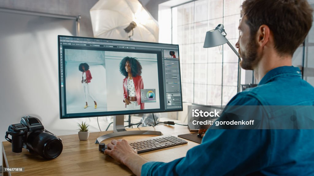 Professioneller Fotograf, der an seinem Schreibtisch sitzt, verwendet Desktop-Computer in einem Fotostudio Retusch. Nach dem Fotoshooting retuschiert er Fotos von schönem schwarzen weiblichen Modell in einer Bildbearbeitungssoftware - Lizenzfrei Fotografisches Bild Stock-Foto