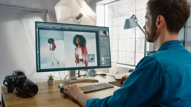 Photo of Professional Photographer Sitting at His Desk Uses Desktop Computer in a Photo Studio Retouches. After Photoshoot He Retouches Photographs of Beautiful Black Female Model in an Image Editing Software