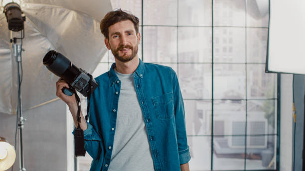 en el estudio de fotos con equipo profesional: retrato del guapo fotógrafo que sostiene la cámara de estado de la técnica listo para tomar fotos con iluminación softboxes en segundo plano - handsome man flash fotografías e imágenes de stock