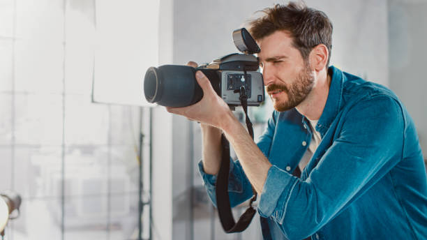 retrato de un fotógrafo famoso, tomando fotos con cámara profesional. elegante revista de moda photo shoot hecho en un estudio. - handsome man flash fotografías e imágenes de stock