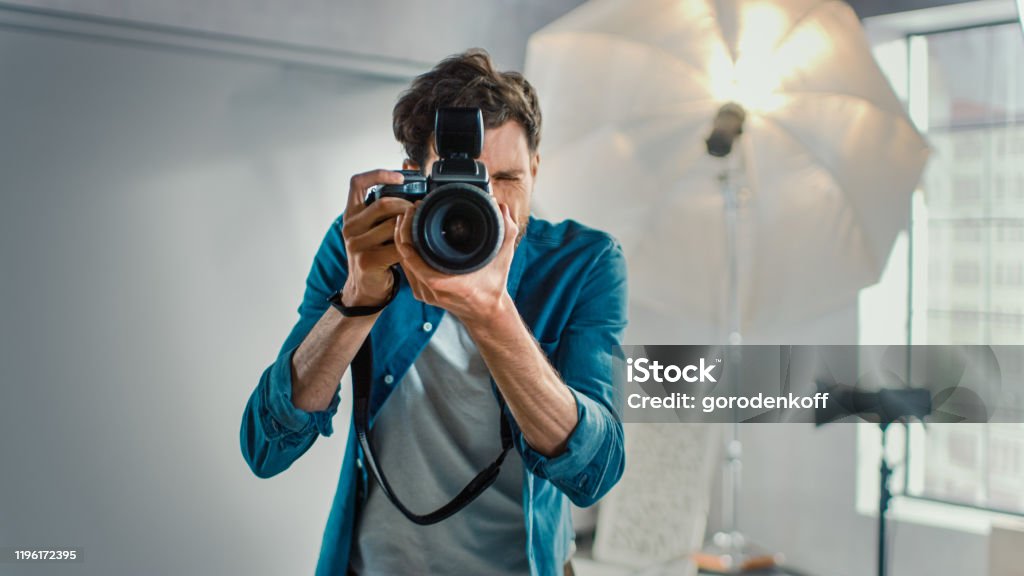 Im Fotostudio mit professioneller Ausstattung: Portrait of the Famous Photographer Holding State of the Art Camera Taking Pictures with Softboxes Flashing in Background. - Lizenzfrei Fotograf Stock-Foto