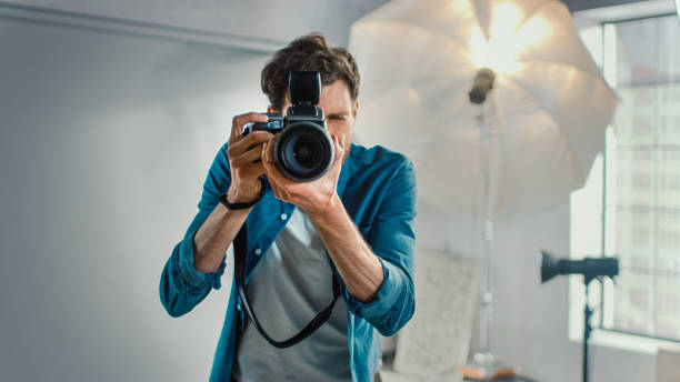 dans le studio de photo avec l'équipement professionnel : portrait du photographe célèbre tenant l'état de l'appareil-photo d'art prenant des images avec des softboxes clignotant en arrière-plan. - photographie photos et images de collection
