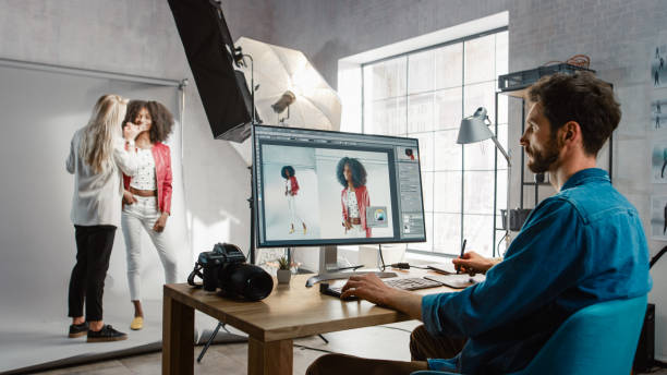 写真撮影の舞台裏:メイクアップアーティストは美しい黒い女の子にメイクアップを適用します。フォトエディタは、画像編集ソフトウェアで写真をレタッチデスクトップコンピュータ上で動 - colorist ストックフォトと画像