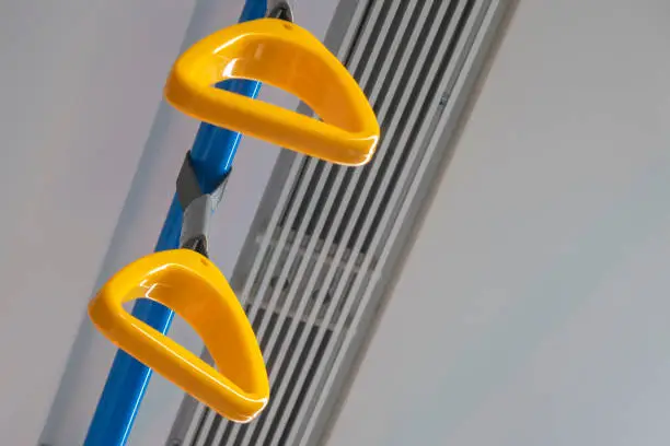 Hanging safety grab handles in public transport. Orange handle and blue handrail. Safety straps. Selective focus.