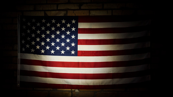 American flag in spotlight hangs on brick wall.