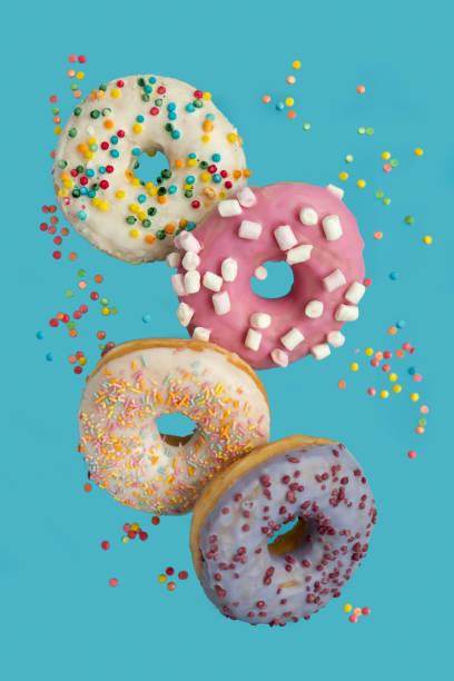 istock Several donuts decorated marshmallow and colorful sprinkles flying on blue background. Flat lay. Top view. Unhealthy food 1196185178