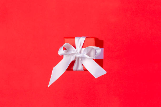 istock Red gift box with white satin ribbon bow flying on red background. Minimal concept for christmas holidays, birthday, valentine, shopping and sales. 1196190986