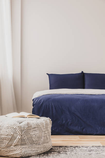istock Empty bedroom interior with simple blue bed and book on pouf, copy space on the wall 1196193594