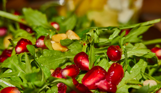 Close-up of red pomegranate seeds on green ruccola leaves, starter with a dressing of grenadine, lemon juice and walnut oil