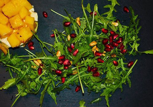 Starter of a rocket salad with pomegranate seeds on a layered salad of avocado, mozarella and mango, dressing of the starter of lime juice with nut oil and grenadine