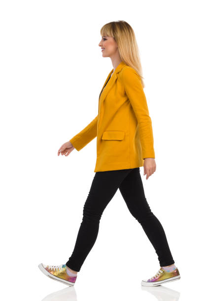 Young Woman In Yellow Jacket And Sneakers Is Walking. Side View. stock photo