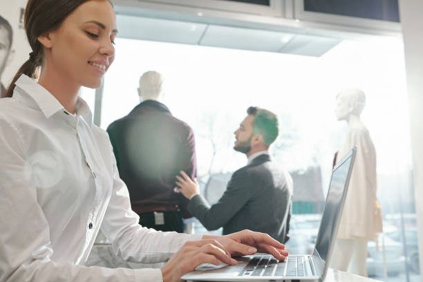 istock Young smiling shop assistant looking through online assortment on laptop screen 1196199513