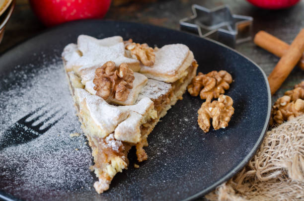 Slice of fresh baked homemade apple pie and walnuts on the black plate