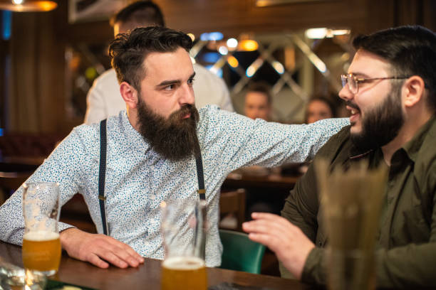 バーカウンターに座ってビールを飲みながら話すヒップスターの友人 - drinking couple bar counter bar ストックフォトと画像