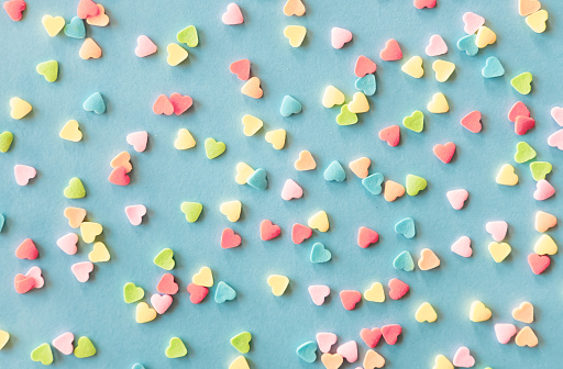 Colorful sugar heart shaped sprinkles frame on green blue background. Valentines day concept.