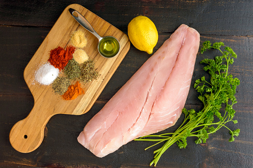 Raw snapper fillet, dried spices, and other ingredients to make a Cajun fish recipe