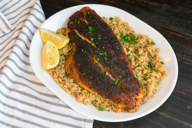 Cajun-style Blackened Red Snapper on Dirty Rice Blackened red snapper fillet served on a platter of dirty rice with lemon wedges and parsley garnish cajun food photos stock pictures, royalty-free photos & images