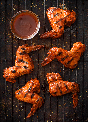 Barbecue grilled chicken wings with a side of barbecue sauce on a dark background