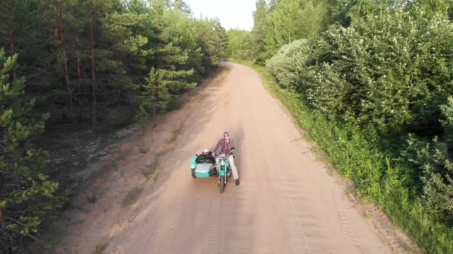 Sidecar retro motorcycle man kickstart and ride with girl on unpaved road aerial high angle