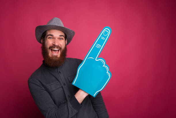 istock Young joyful man pointing away at copyspace with fan glove 1196258268