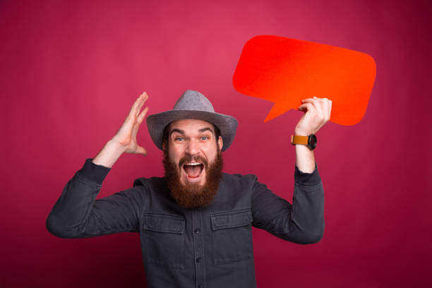 istock Shocked young bearded hipster man holding speech bubble and gesturing 1196258315