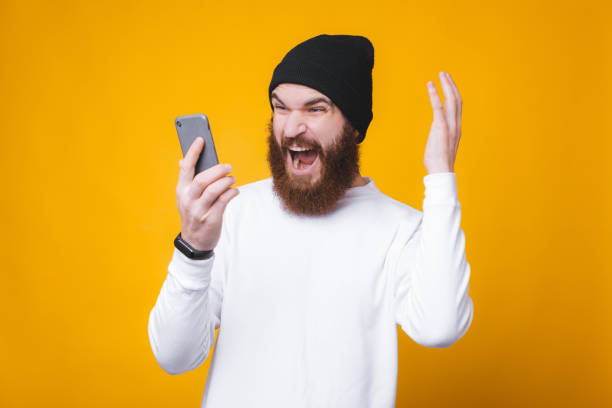 istock Angry man with beard screaming on smartphone, talking on phone with someone 1196258514