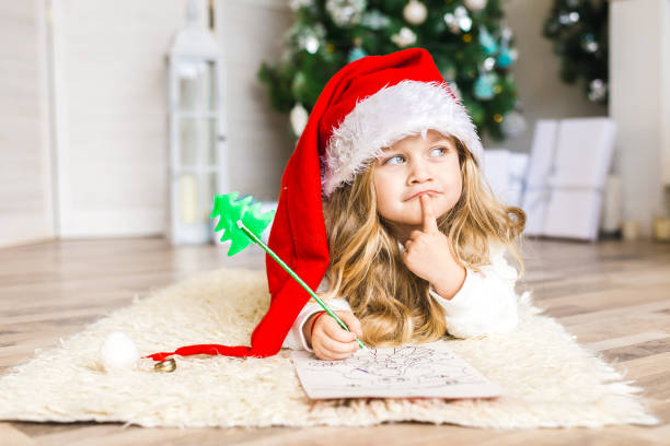 bambina con cappello babbo natale scrive lettera a babbo natale - christmas child foto e immagini stock